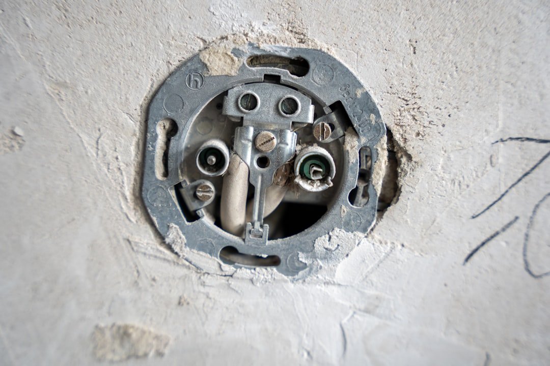 A close-up view of an uncovered wall socket during electrical installation, with exposed wires and mounting plate embedded in rough plaster. The image highlights the technical and tactile aspects of renovation work.